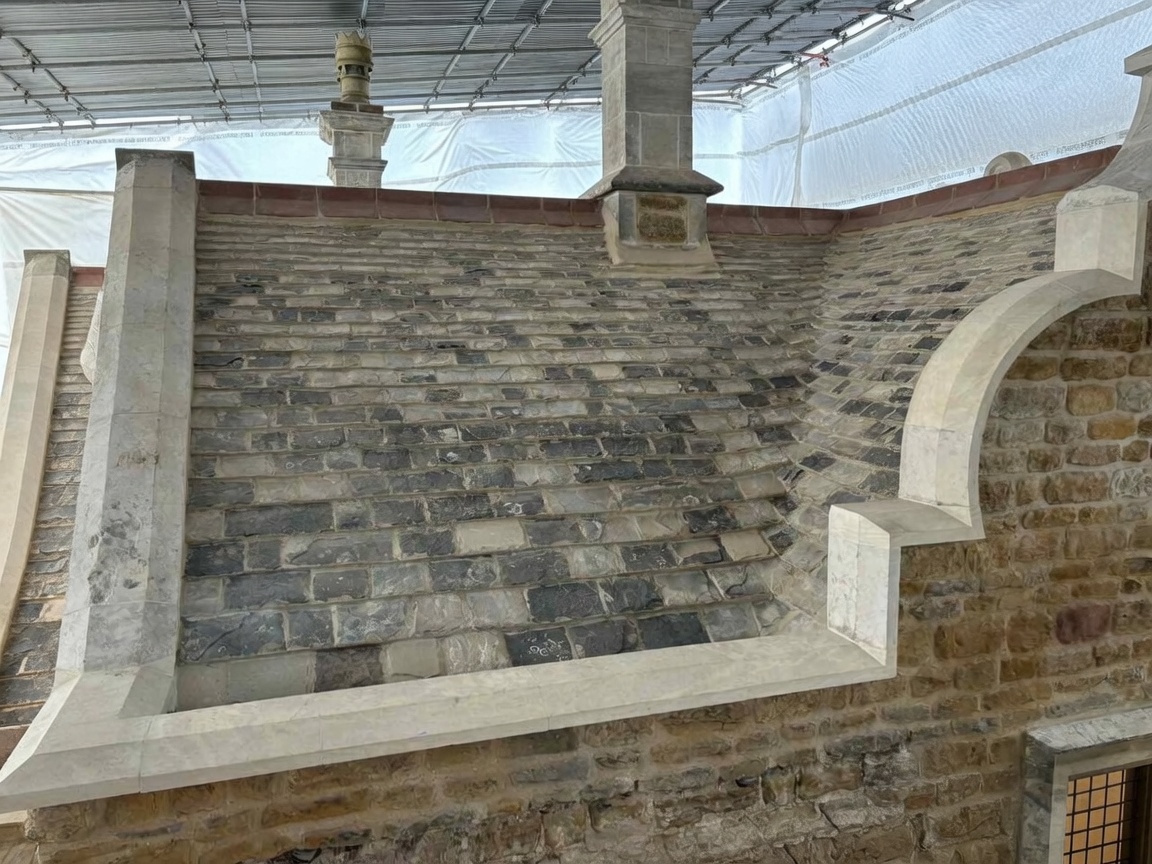 Conservation rebuild of a coursed limestone and ironstone wall with new dressed copings, kneelers and a shaped stone arch, worked under a temporary scaffold roof