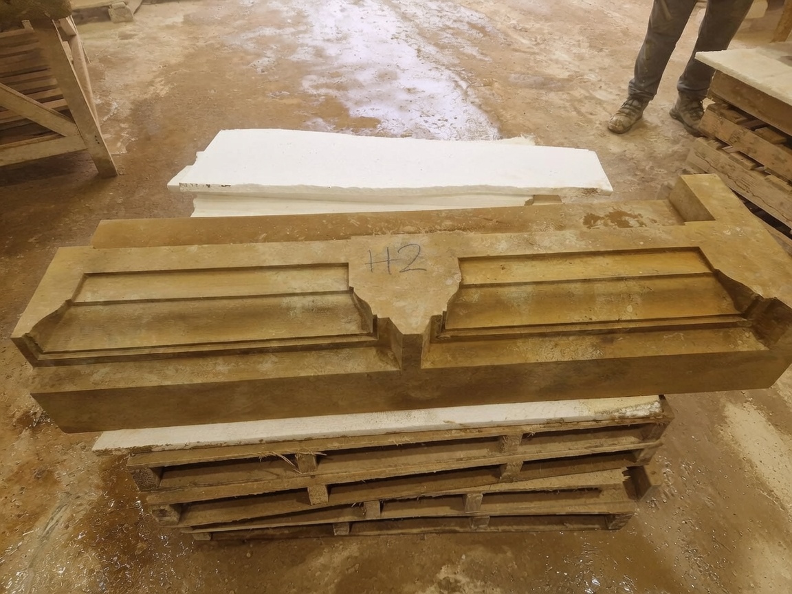 Hand-cut limestone door head with moulded panels and a shaped keystone, laid out on pallets in the masonry workshop