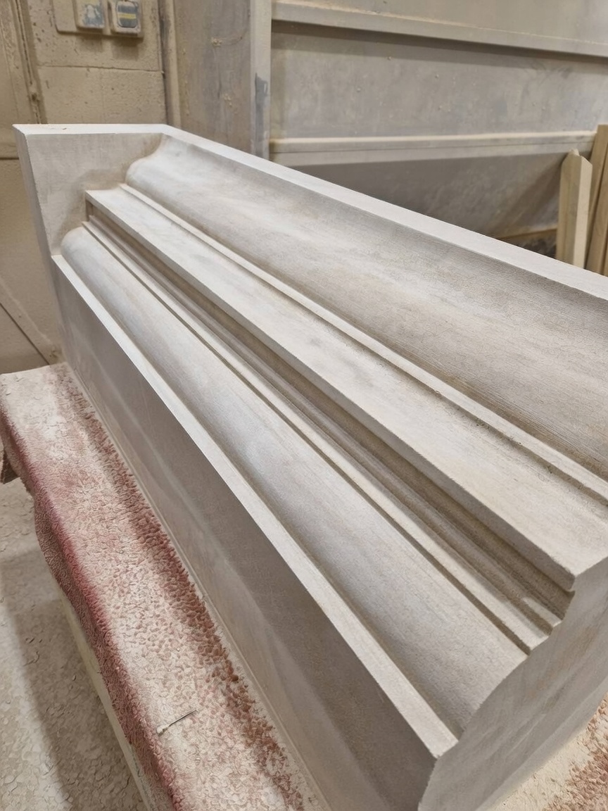 Hand-worked limestone cornice section with deep mouldings and crisp arrises, resting on a padded banker bench in the masonry workshop