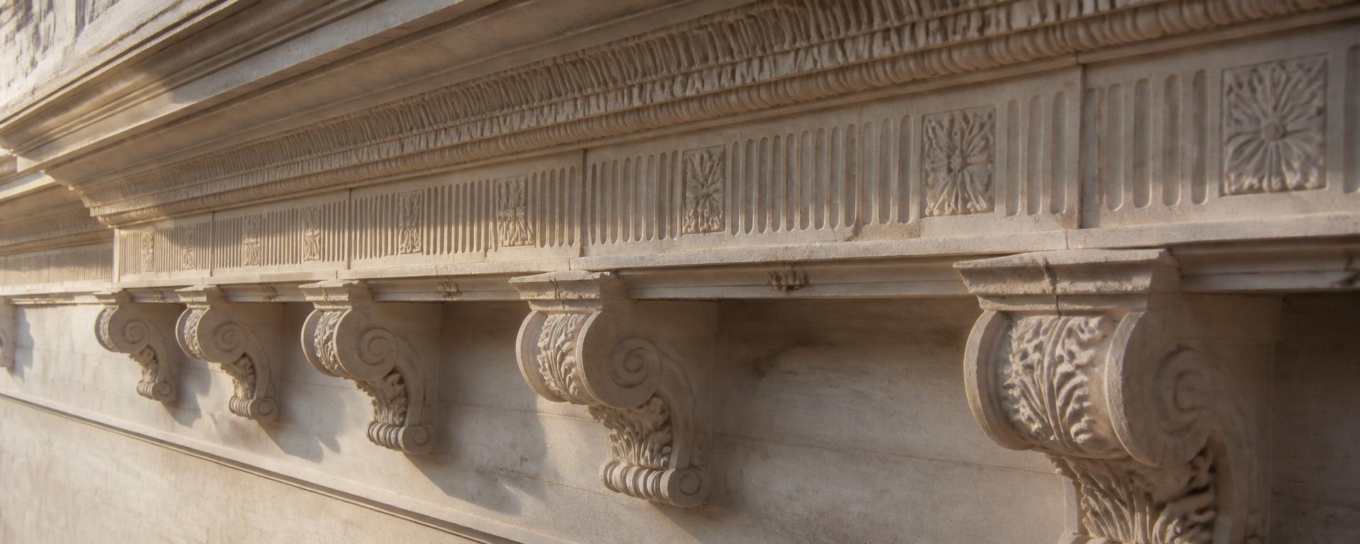 Hand-carved limestone cornice, enriched frieze and moulded corbels running along a classical stone facade