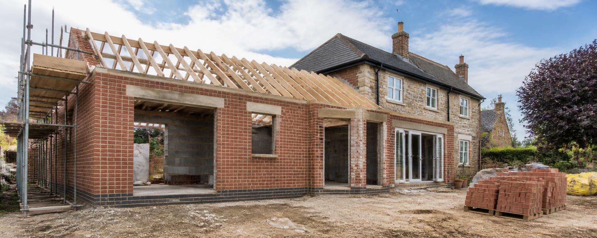 Brick and stone house extension under construction with new roof timbers, neat brickwork and a tidy working site