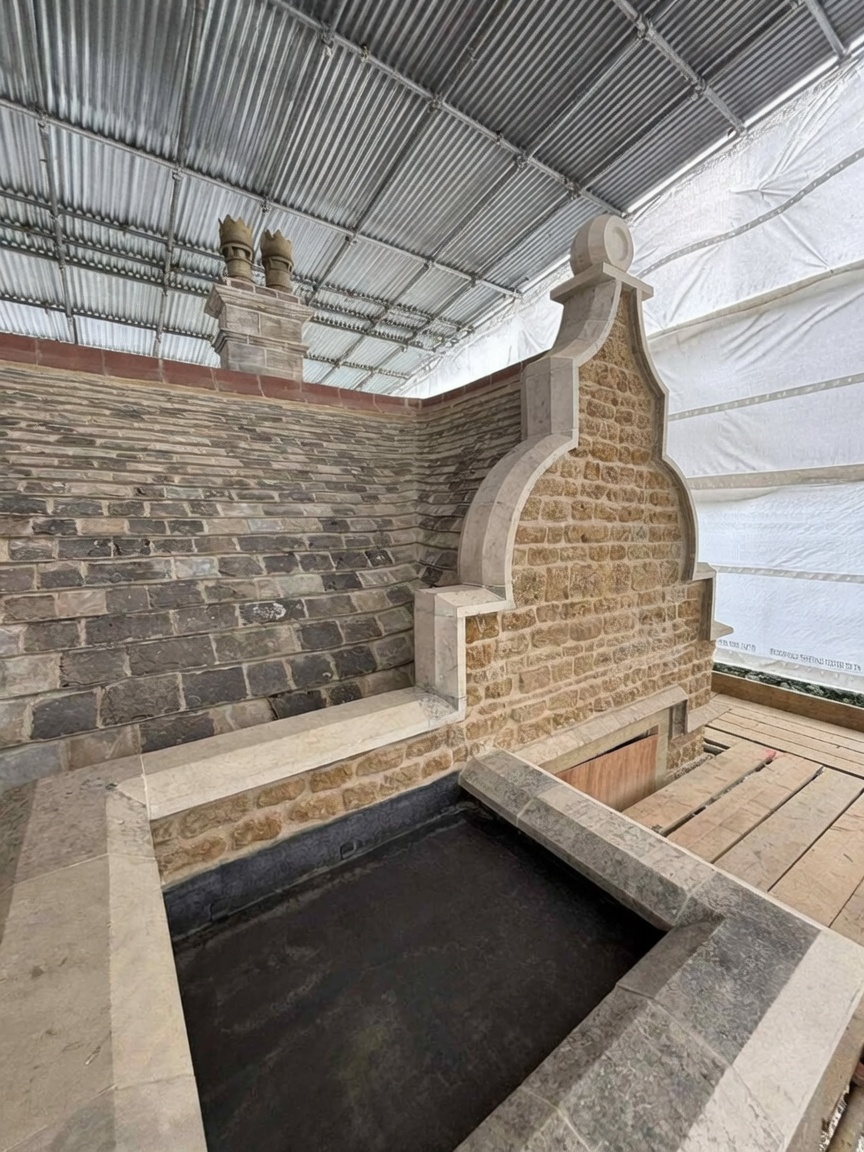 Restored historic stone gable and parapet at Nevill Holt, with rebuilt coursed walling, carved stone coping, shaped kneelers and a chimney stack under a temporary scaffold roof.