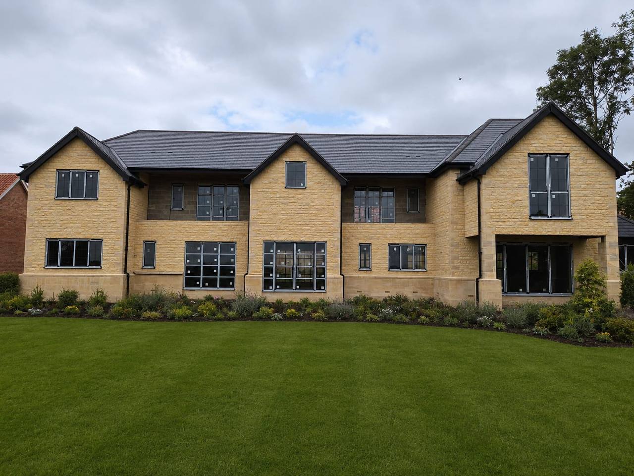 Large new build country house faced in coursed golden limestone with ashlar quoins, gabled bays and dark slate roofs, set behind a landscaped lawn