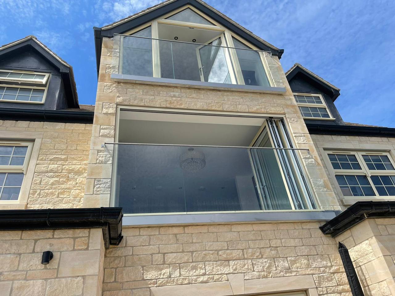 Upper elevation of a new build stone house in rock-faced and ashlar limestone with dressed quoins and glass Juliet balconies to bi-fold openings