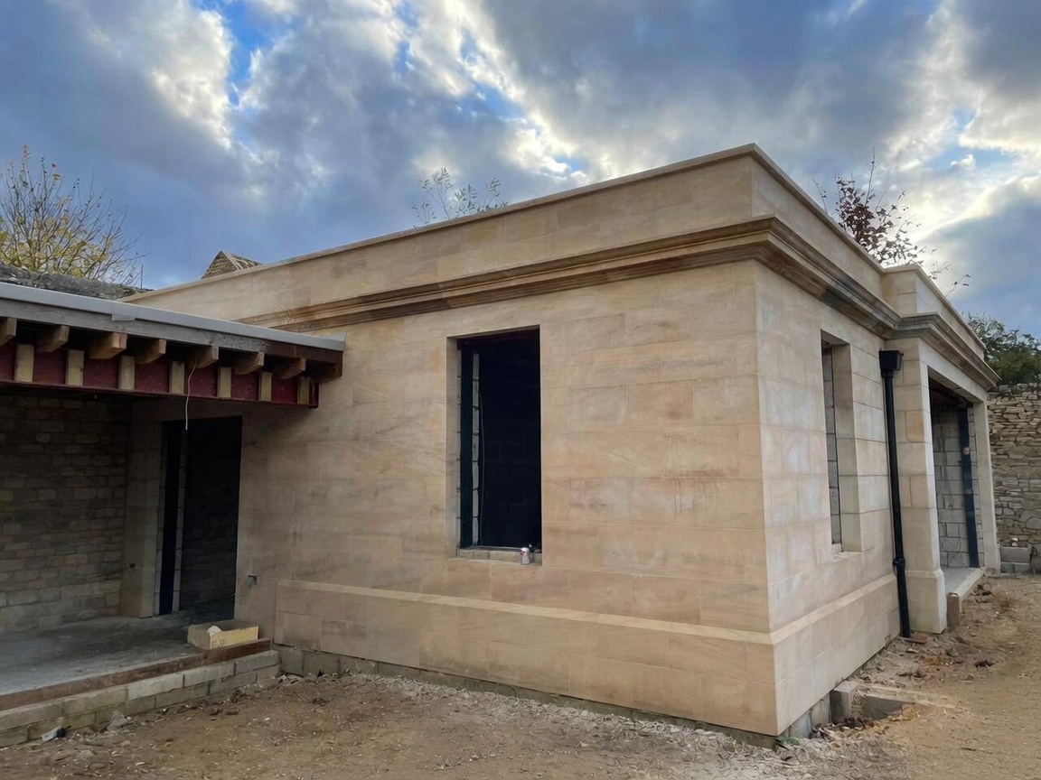 Newly built ashlar sandstone pavilion under a dramatic sky, with fine-jointed walling, a moulded cornice, deep plinth and dressed window openings